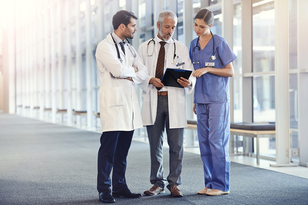 Doctors discussing patient documentation while reviewing a Q-Centrix alternative on a desktop computer in a medical office.
