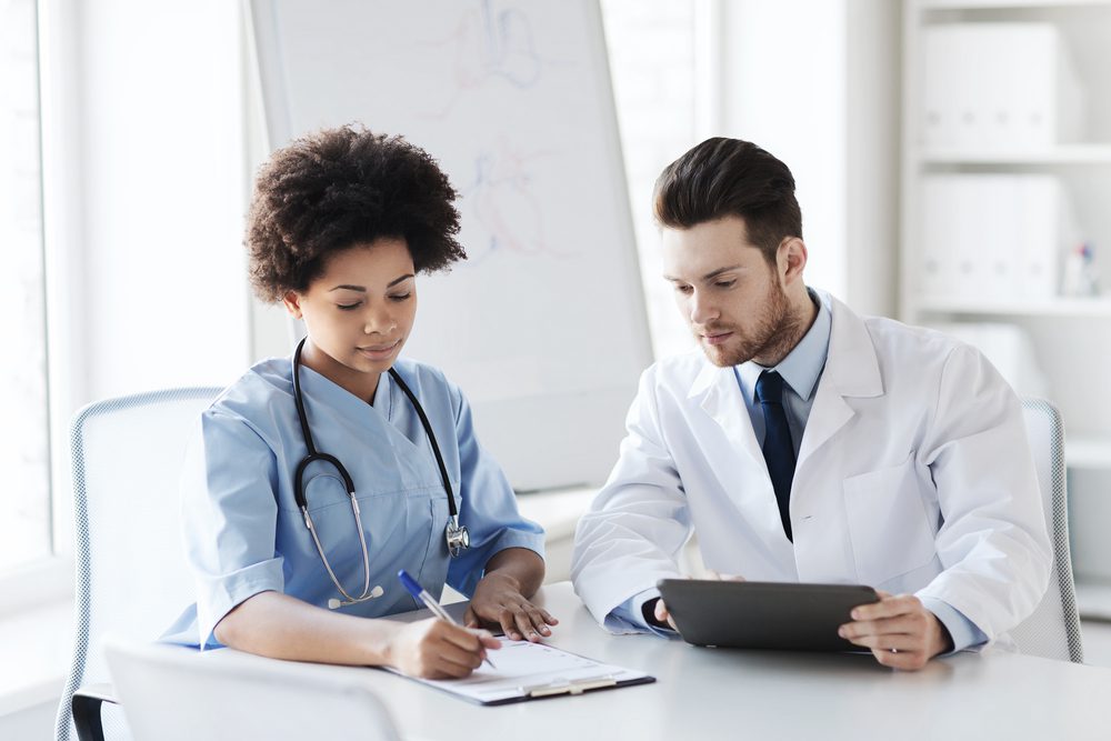 Two physicians collaborating while analyzing clinical data using registry management software at a hospital workstation.
